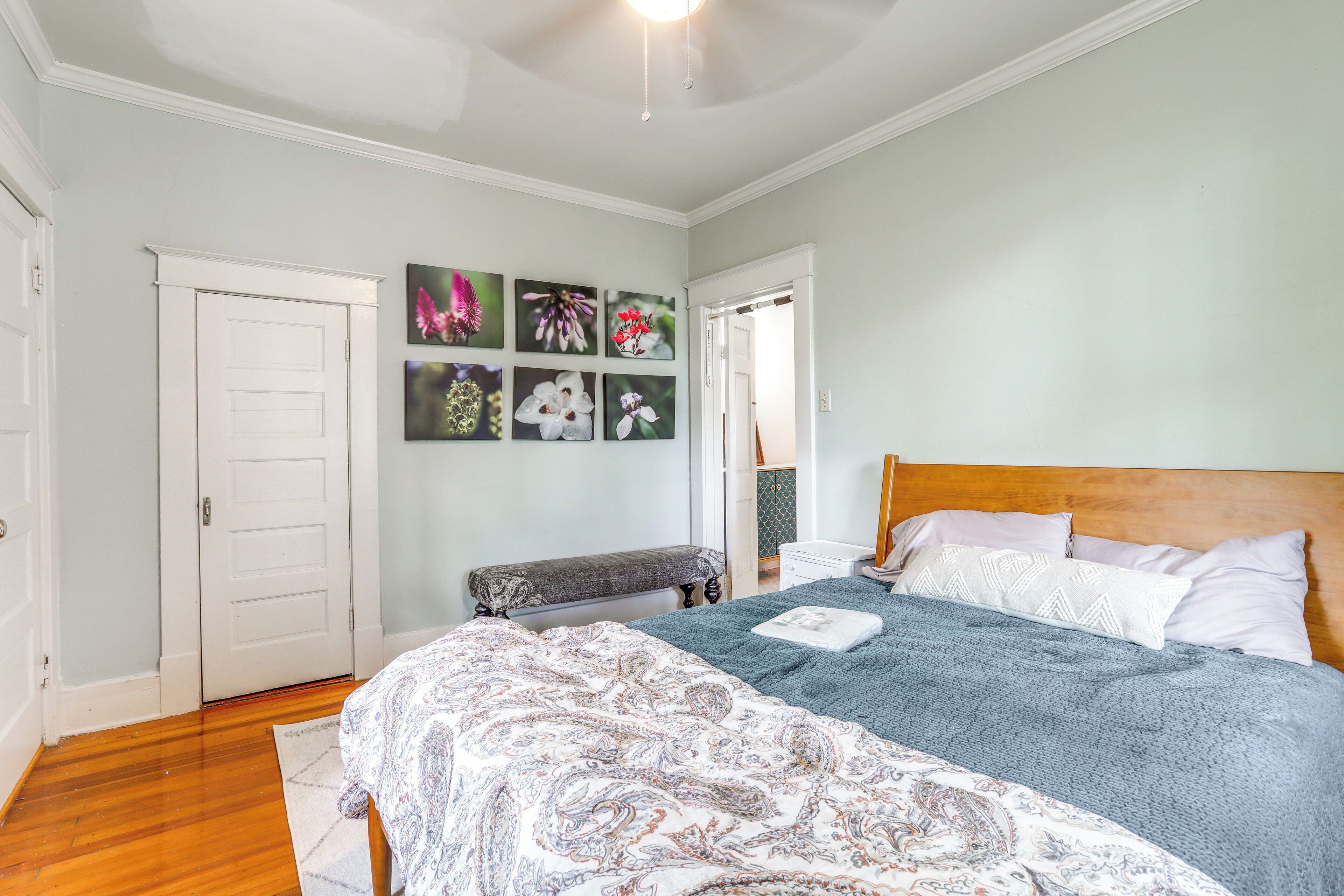 A bedroom with a bed, a bench, a wall with framed pictures, and a door.