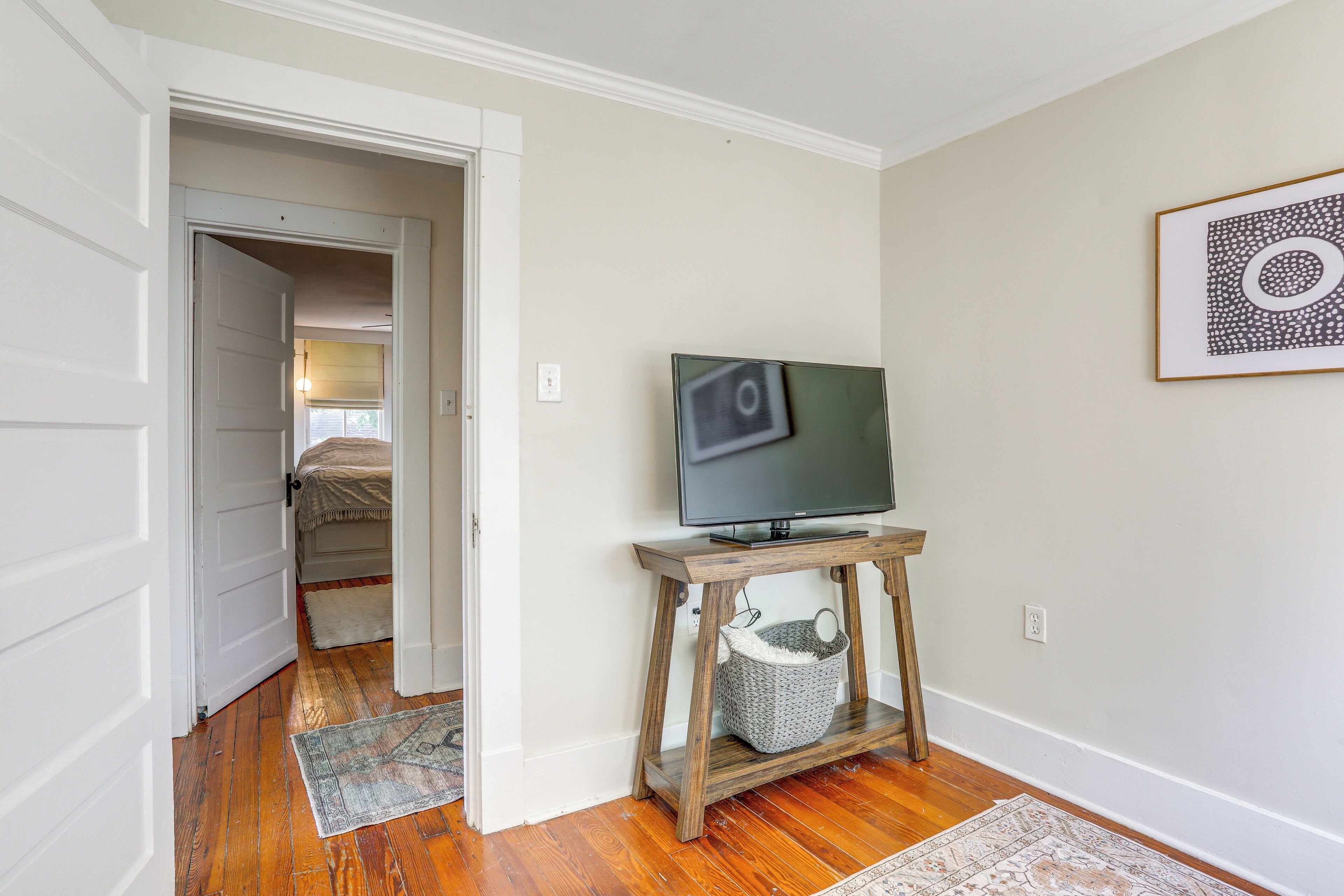 A room with a wooden floor, a television on a wooden stand, a white door, and a framed picture on the wall.