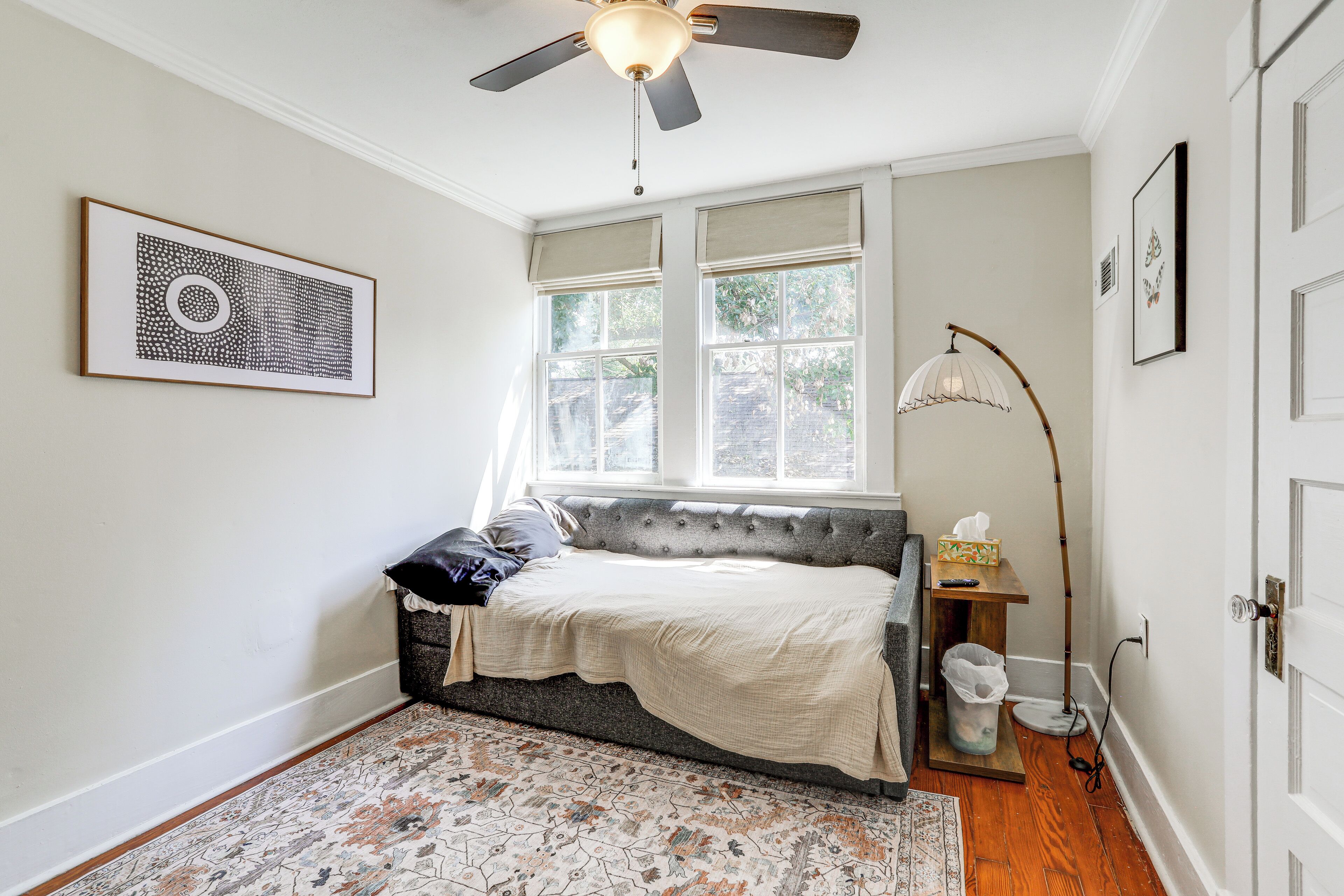 A bedroom with a bed, a ceiling fan, a window with blinds, a floor lamp, and a rug.