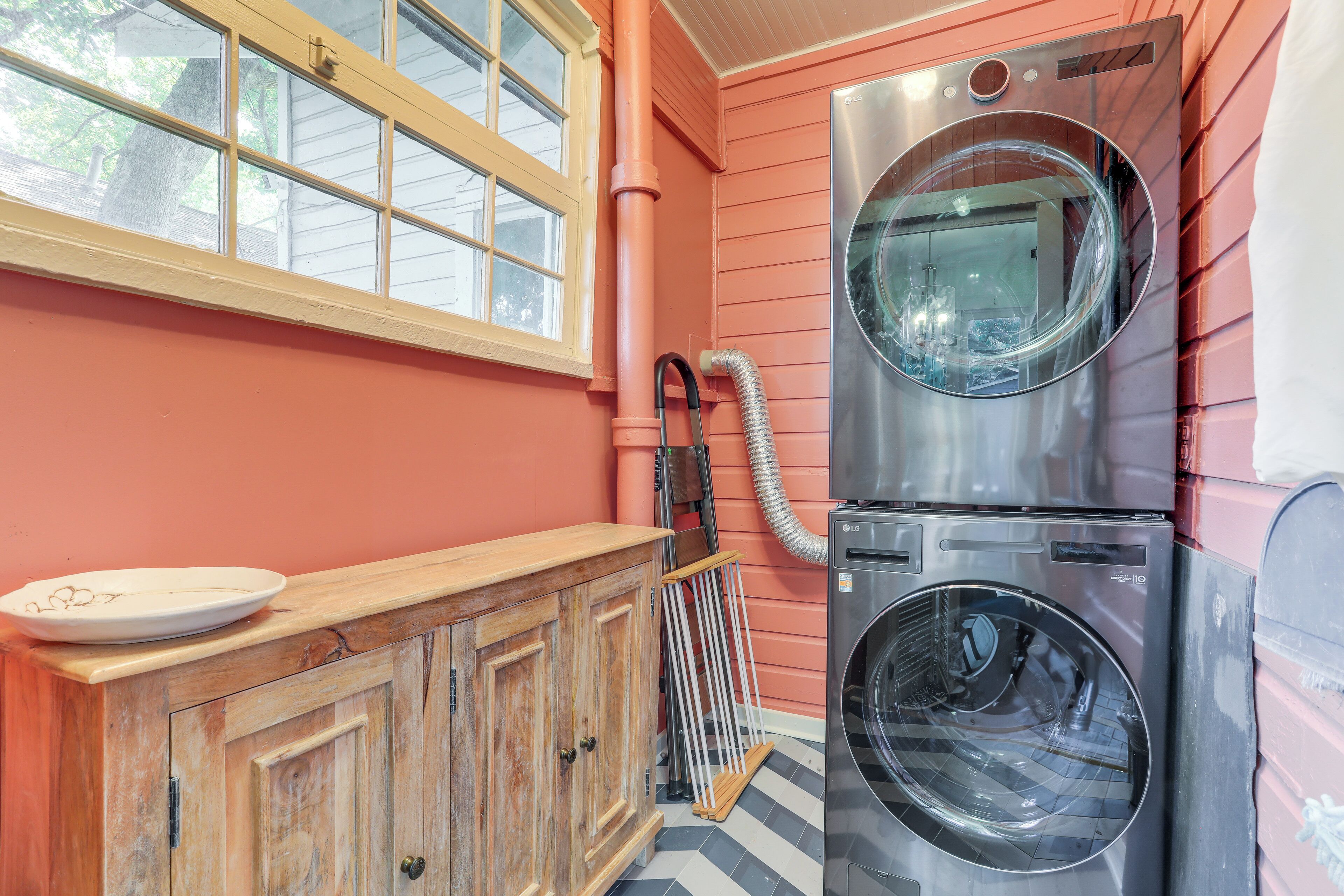 Une buanderie équipée de deux machines à laver et deux sèche-linge superposés, d’un meuble en bois sur lequel est posée une assiette, d’une fenêtre et d’une échelle appuyée contre le mur.