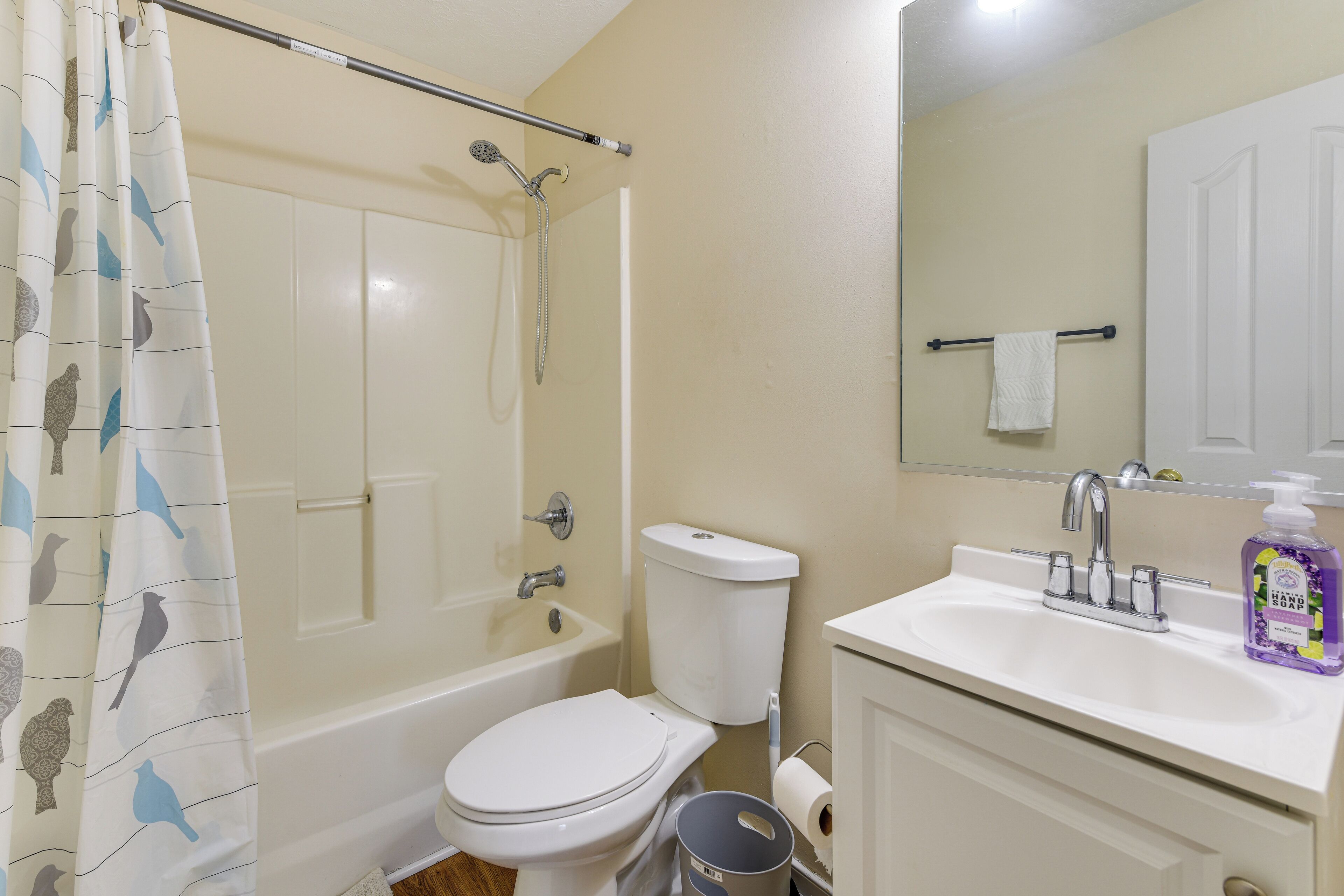 A bathroom with a bathtub, toilet, sink, and a shower curtain with bird patterns.
