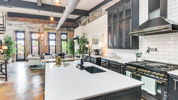 A spacious kitchen with a large island, dark cabinetry, and a brick wall. - Modern Dtwn Condo w/ Balcony in Hendersonville (Hendersonville)