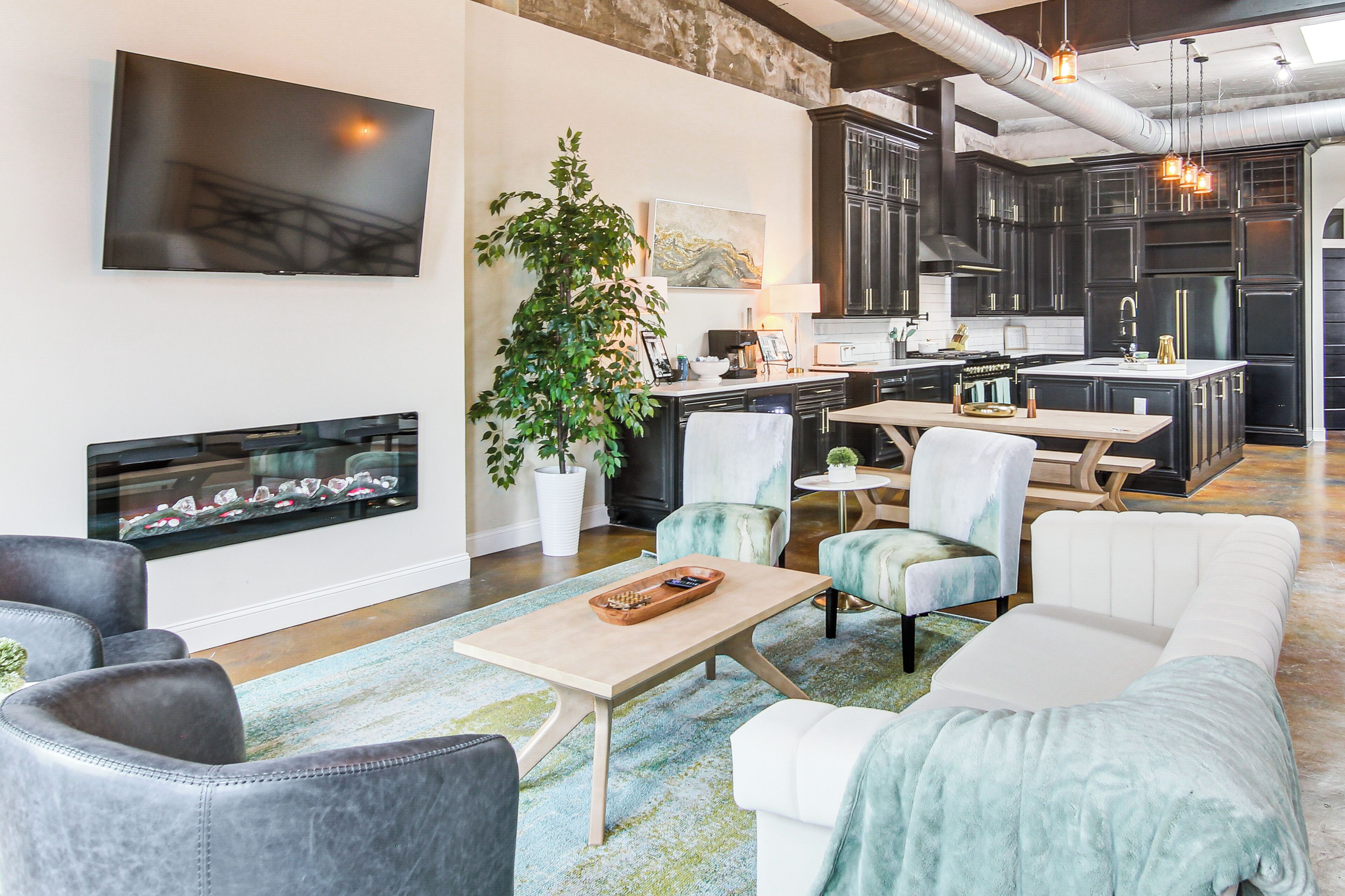 Un salon moderne avec une cheminée, des sièges confortables et une cuisine en arrière-plan.