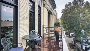An outdoor seating area with a table and chairs, a hanging plant, and a street view with cars and trees. - Modern Dtwn Condo w/ Balcony in Hendersonville (Hendersonville)