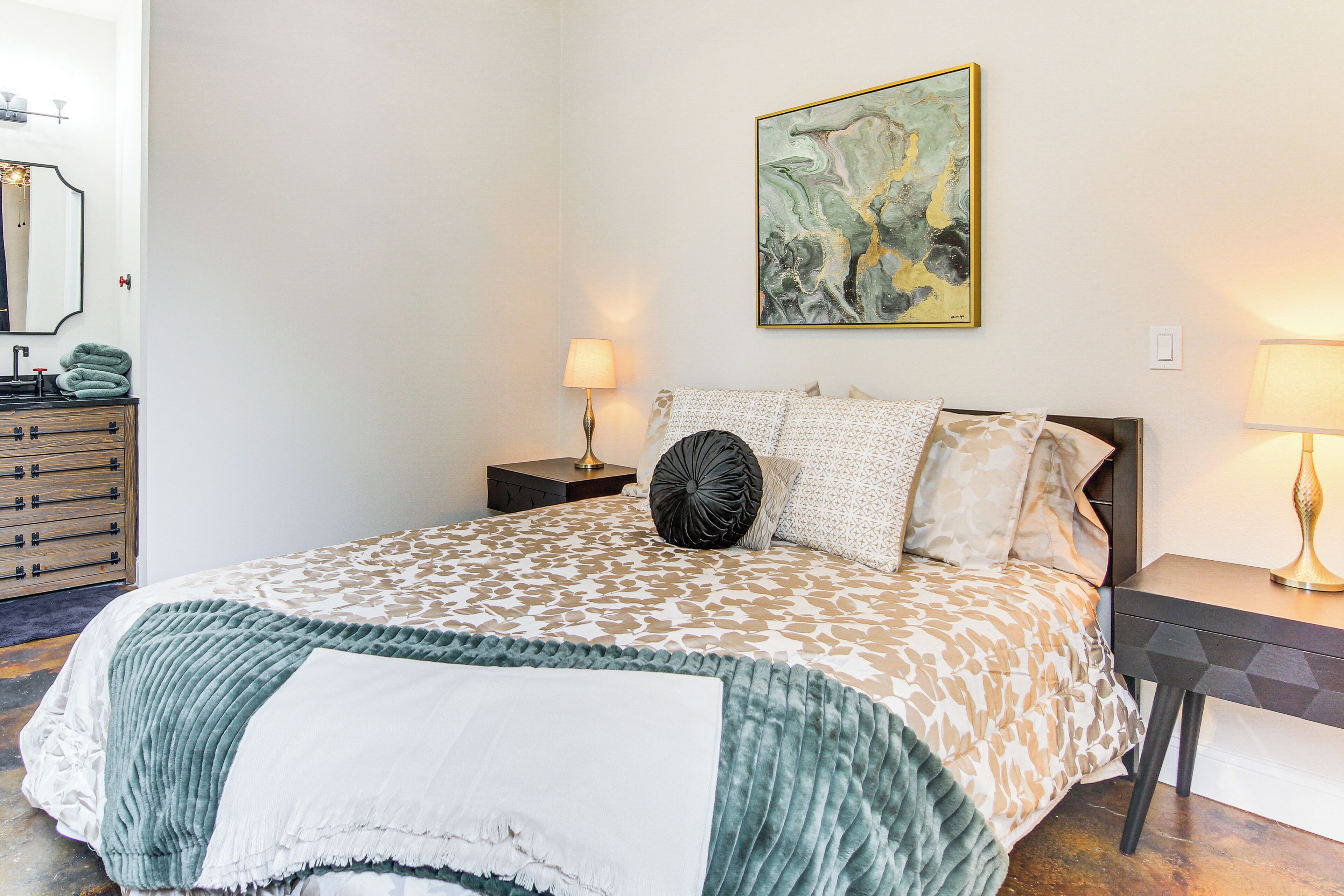Quarto bem arrumado com uma cama grande, uma mesa de cabeceira com abajur, cômoda e um quadro na parede.