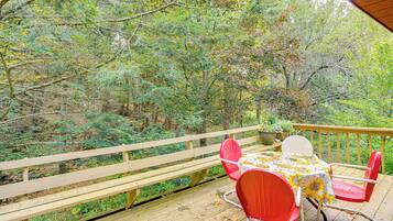 A wooden deck with a table and chairs, surrounded by dense trees.