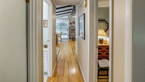 A hallway with wooden flooring, white walls, and a ceiling with exposed beams. There is a chair and a table with a lamp in the room at the end of the hallway. - Quiet All-season Creekside Escape in Upstate! (Berlin)