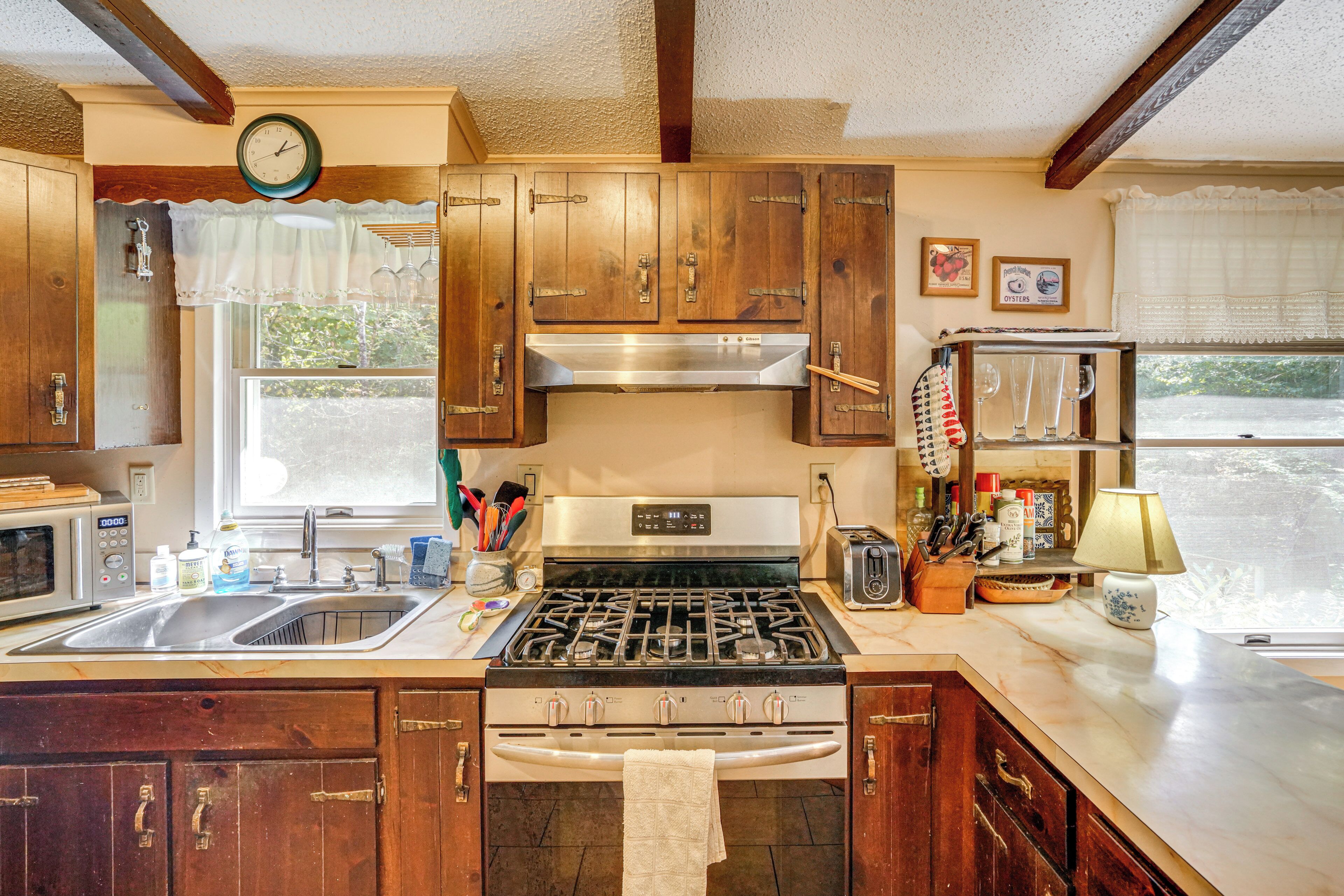 A kitchen with wooden cabinets, a stainless steel range, a microwave, and a window with a view of greenery.