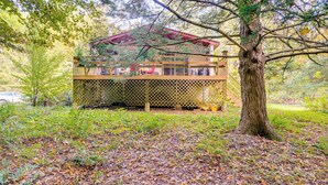 A cabin with a wooden deck, surrounded by trees and a leaf-covered ground. - Quiet All-season Creekside Escape in Upstate! (Berlin)