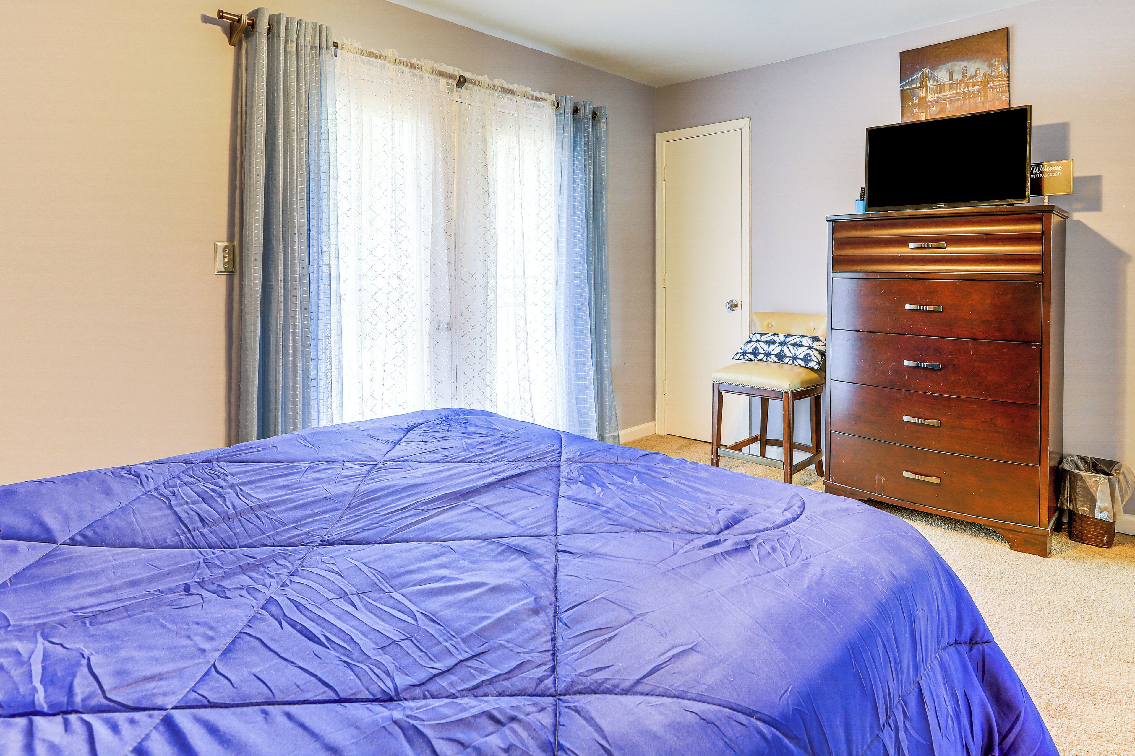 Un dormitorio con una cama grande, un aparador de madera, un televisor encima y una silla.