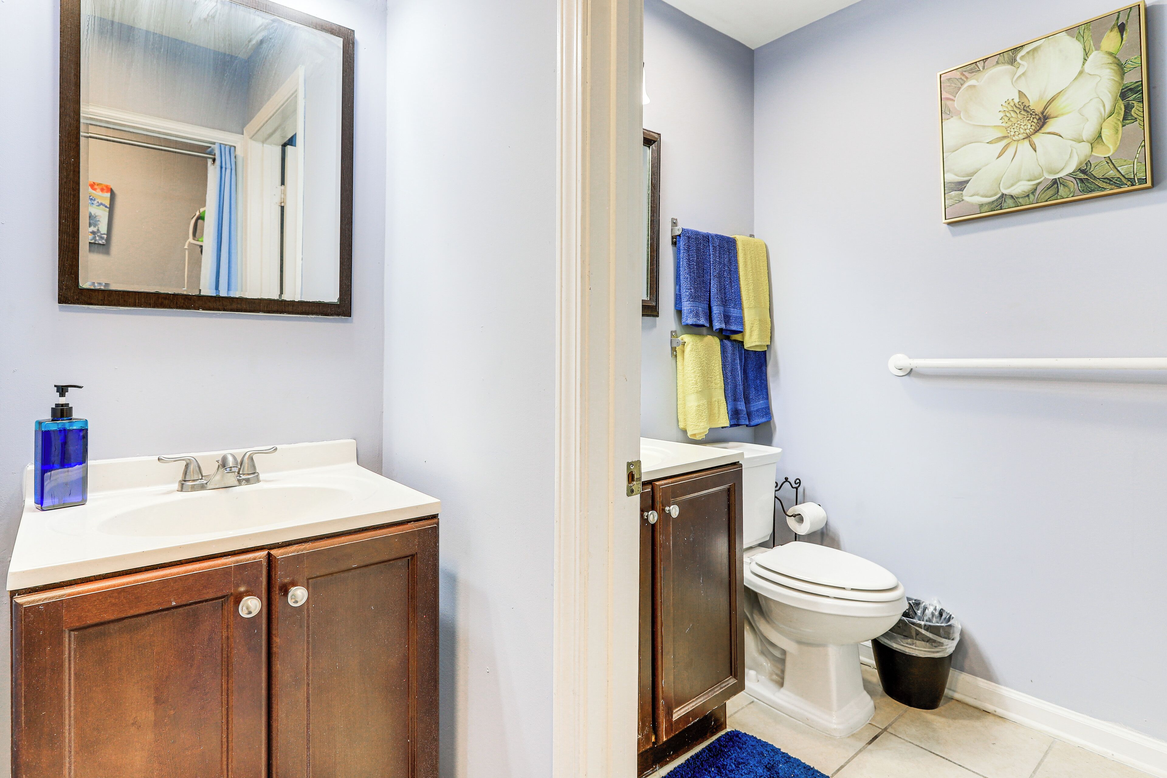 A bathroom with a wooden vanity, a white sink, a mirror, a toilet, and a trash can.