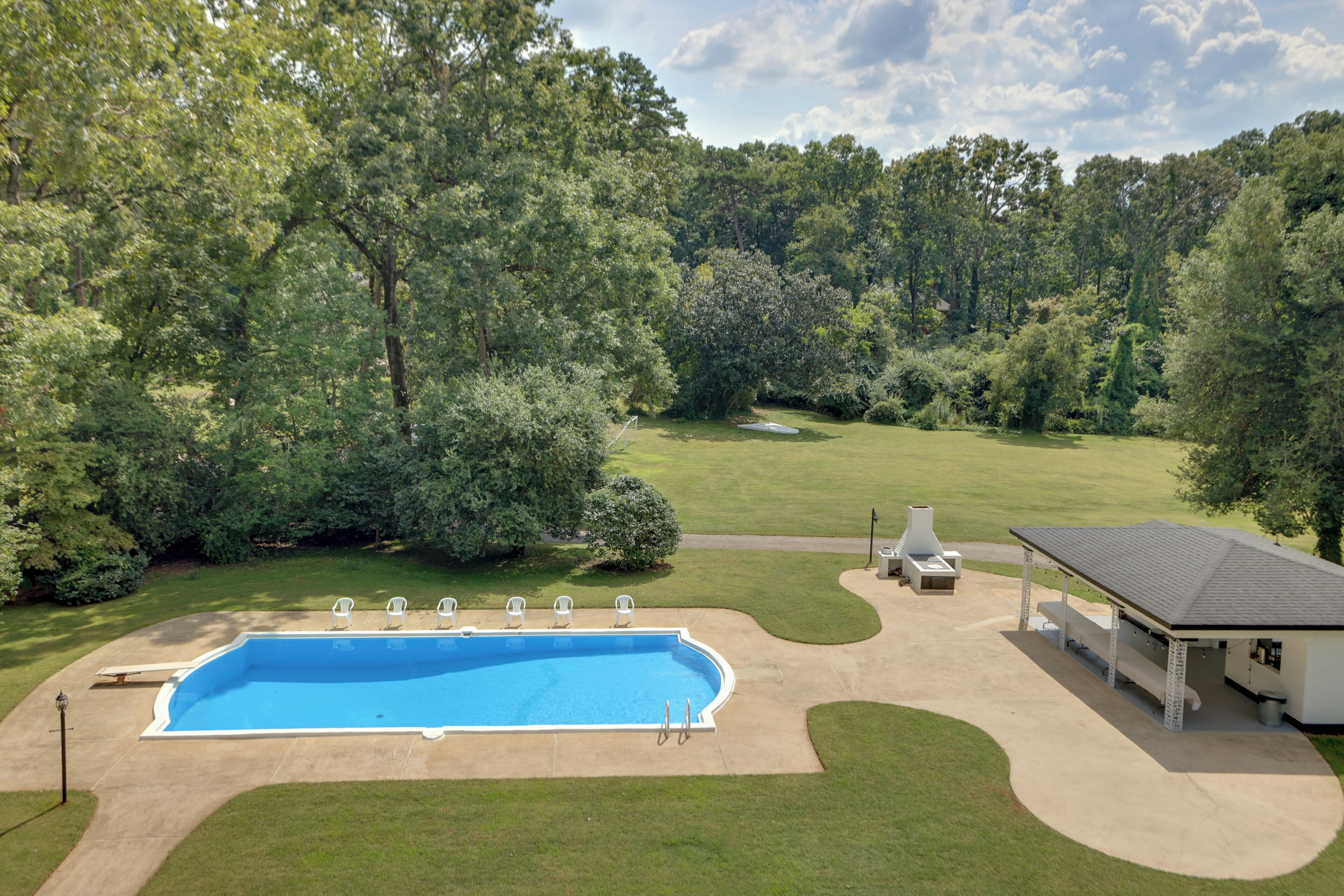 A swimming pool with a deck, surrounded by a lawn and trees.