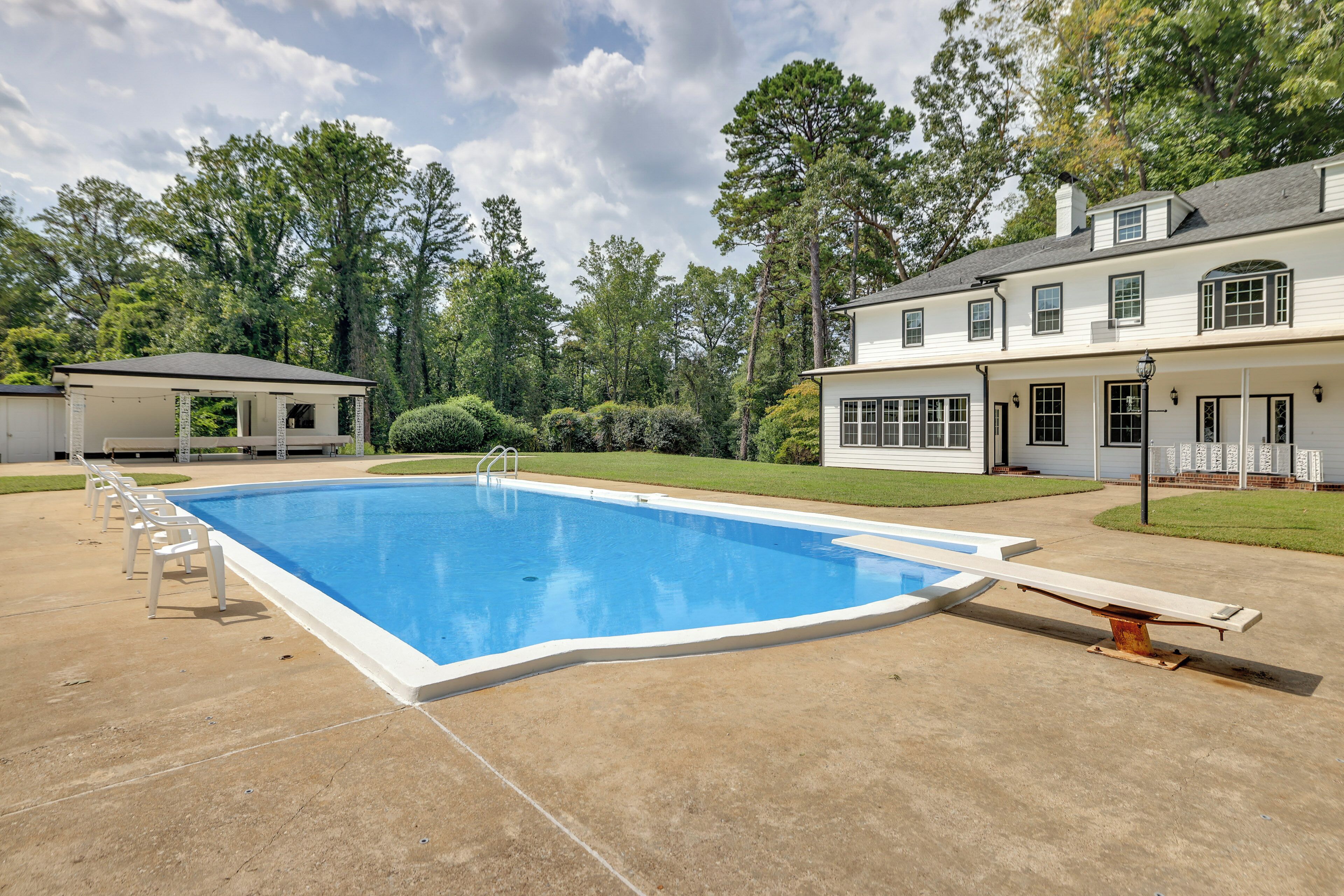 A rectangular swimming pool with a diving board and lounge chairs, surrounded by a well-maintained lawn and trees.