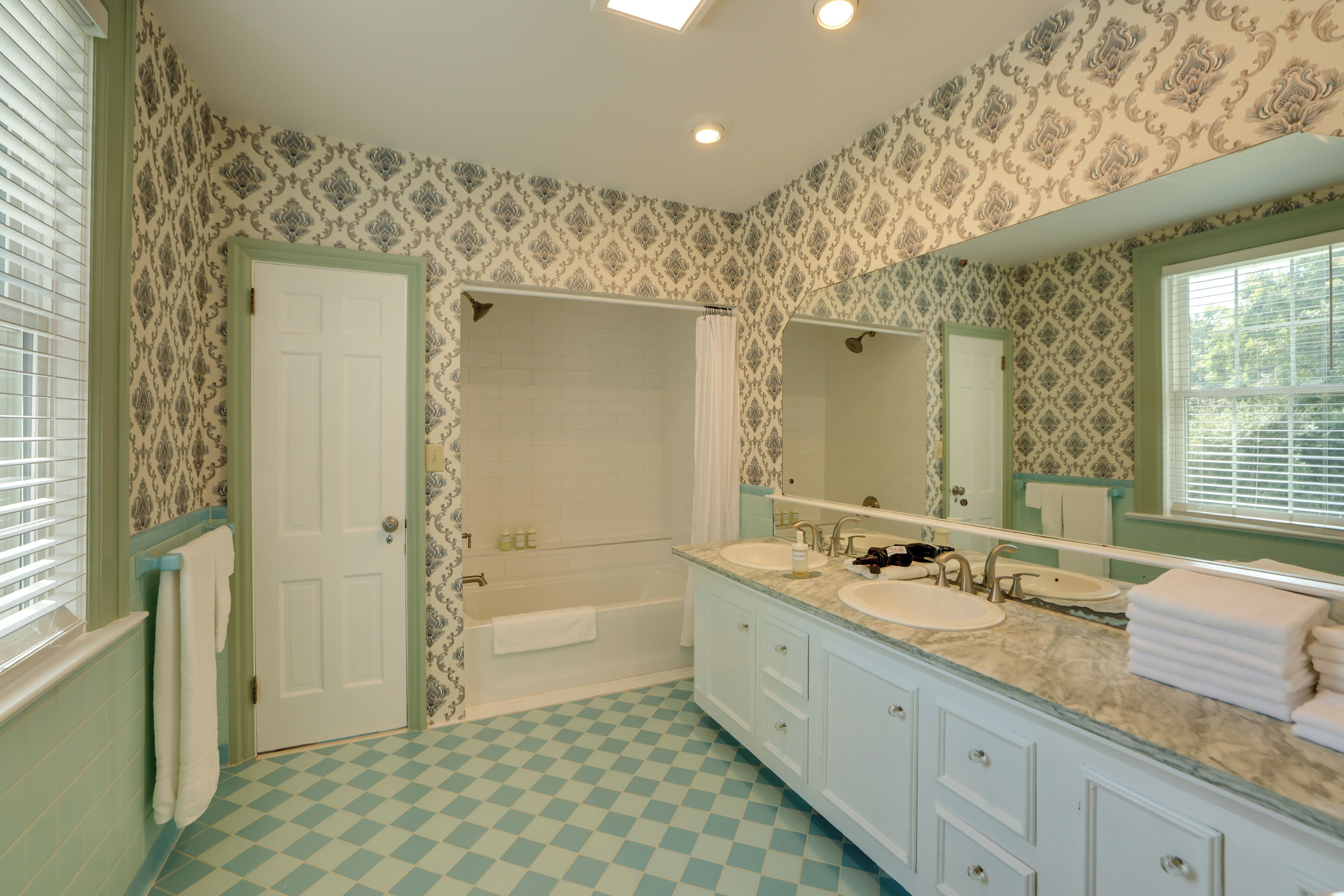 A bathroom with a checkered floor, two sinks, a bathtub, and a large mirror.