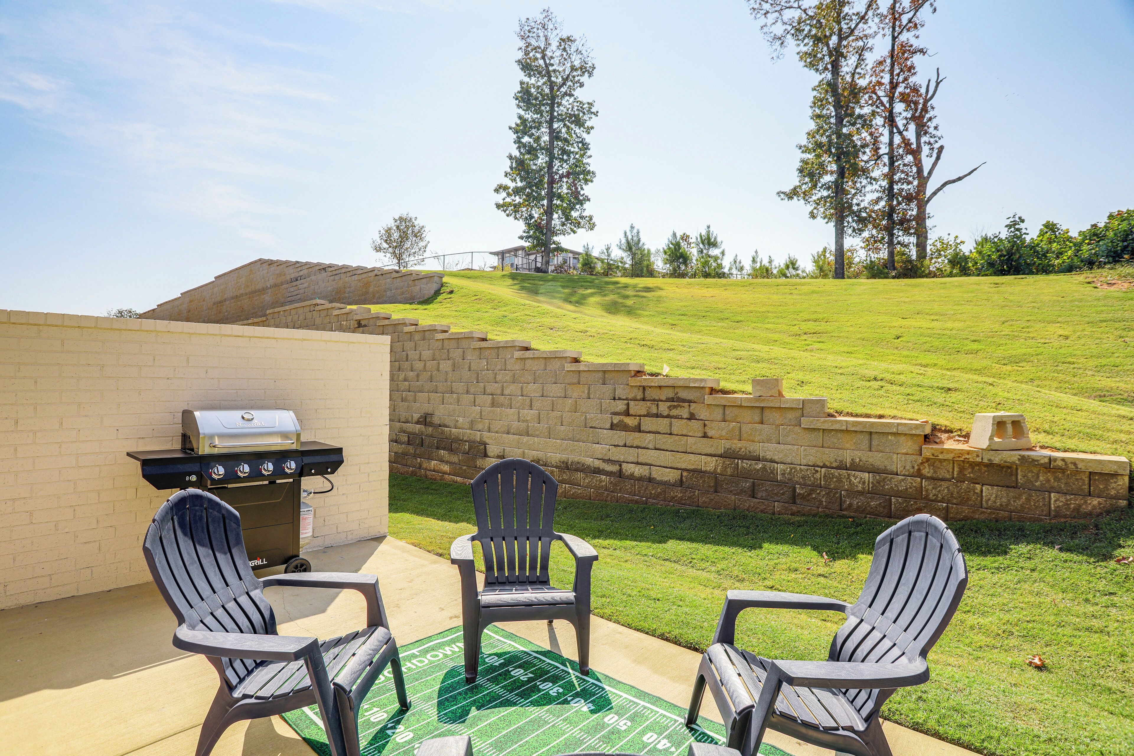 A patio with a grill, two Adirondack chairs, and a green football field mat.