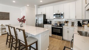 A modern kitchen with white cabinets, stainless steel appliances, and a marble island. - King Suites for Every Couple, Kickoff 3 Mi (Oxford)