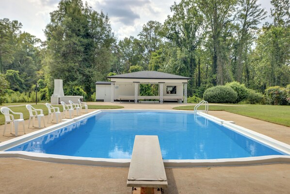 A rectangular swimming pool with a wooden deck in the foreground, surrounded by white plastic chairs and a covered pavilion in the background. - Westwind Estate Apt 6 Mi to Dtwn Spartanburg (Spartanburg)