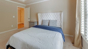 Een slaapkamer met een gebonden hoofdeinde, een groot bed met een beddeken met een patroon, een nachtkastje en een raam met jaloezieën.