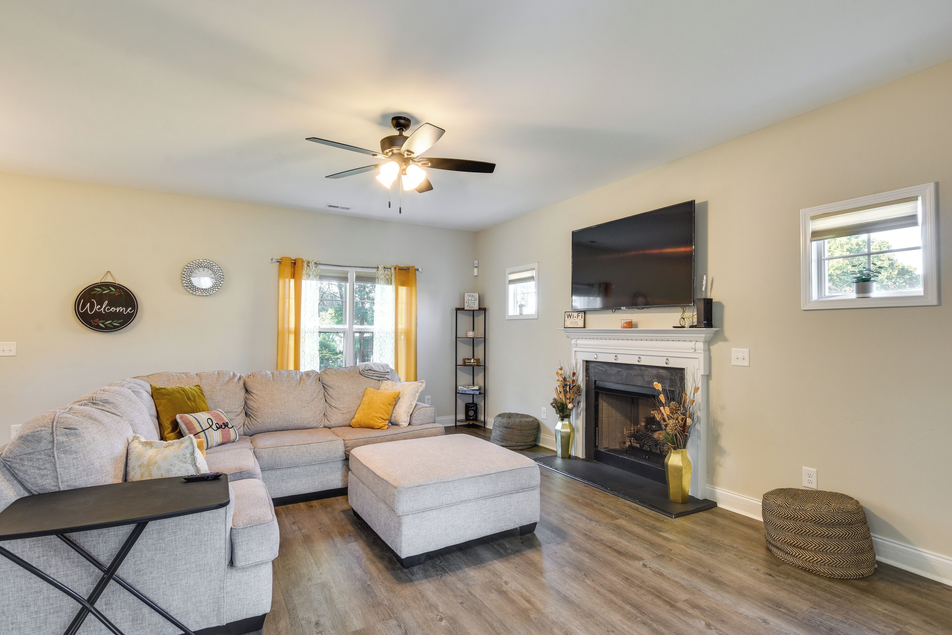 A living room with a sectional sofa, a fireplace, a flat-screen TV, and a ceiling fan.