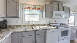 Una cocina con encimeras de granito, un lavamanos doble, microondas, estufa y armarios blancos.