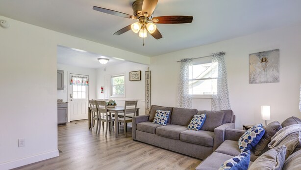 Amplia sala de estar con un sofá gris, un comedor con mesa y sillas de madera, y una cocina al fondo.