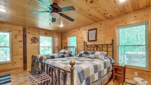 A wooden cabin bedroom with two beds, a ceiling fan, and large windows. - 3 Mi to Dale Hollow Lake: Wooded Retreat w/ Decks! (Byrdstown)