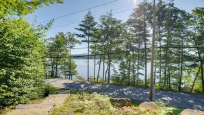 A paved road curving through a forest with a lake and mountains in the background. - Walk to Lake Winnisquam Access: Cozy Retreat (Sanbornton)