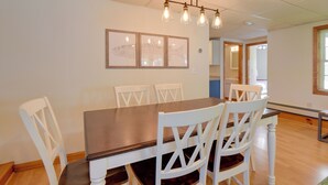 A dining area with a wooden table and white chairs, framed artwork on the wall, and a ceiling light fixture. - Walk to Lake Winnisquam Access: Cozy Retreat (Sanbornton)