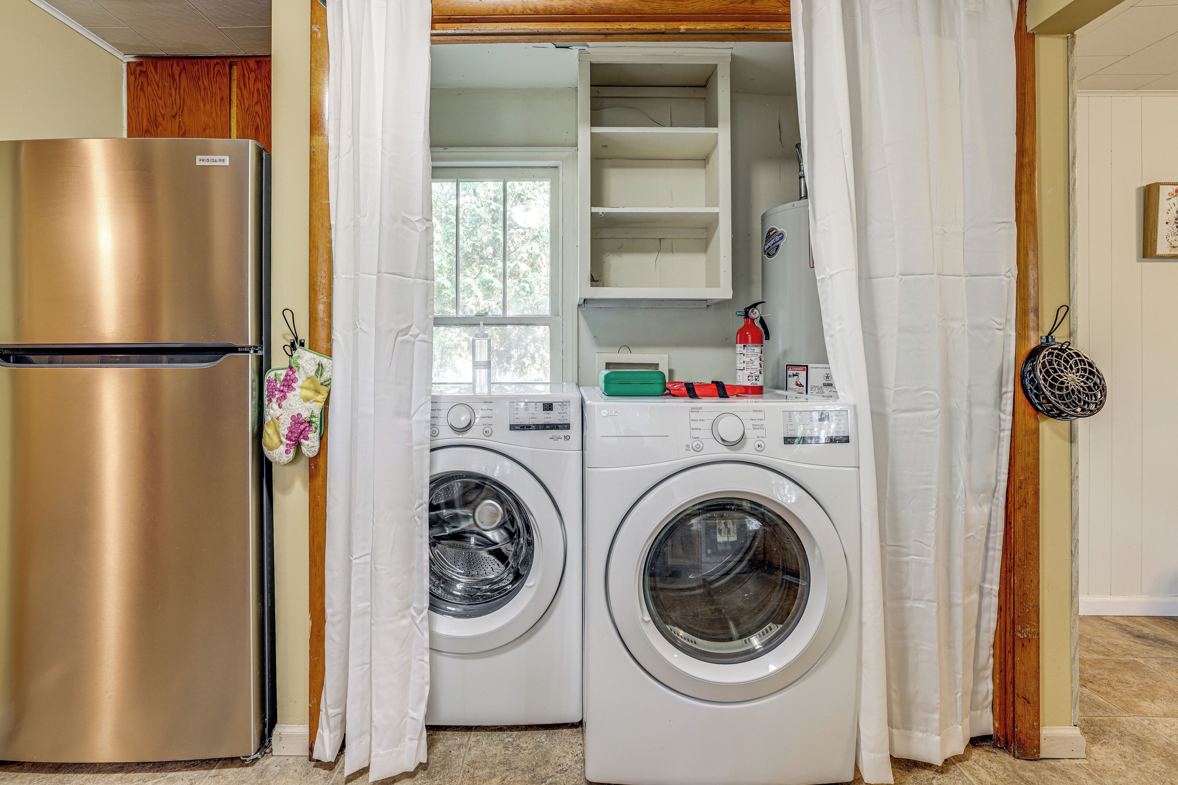 A laundry area with a stainless steel refrigerator, two front-loading washing machines, and a drying rack.