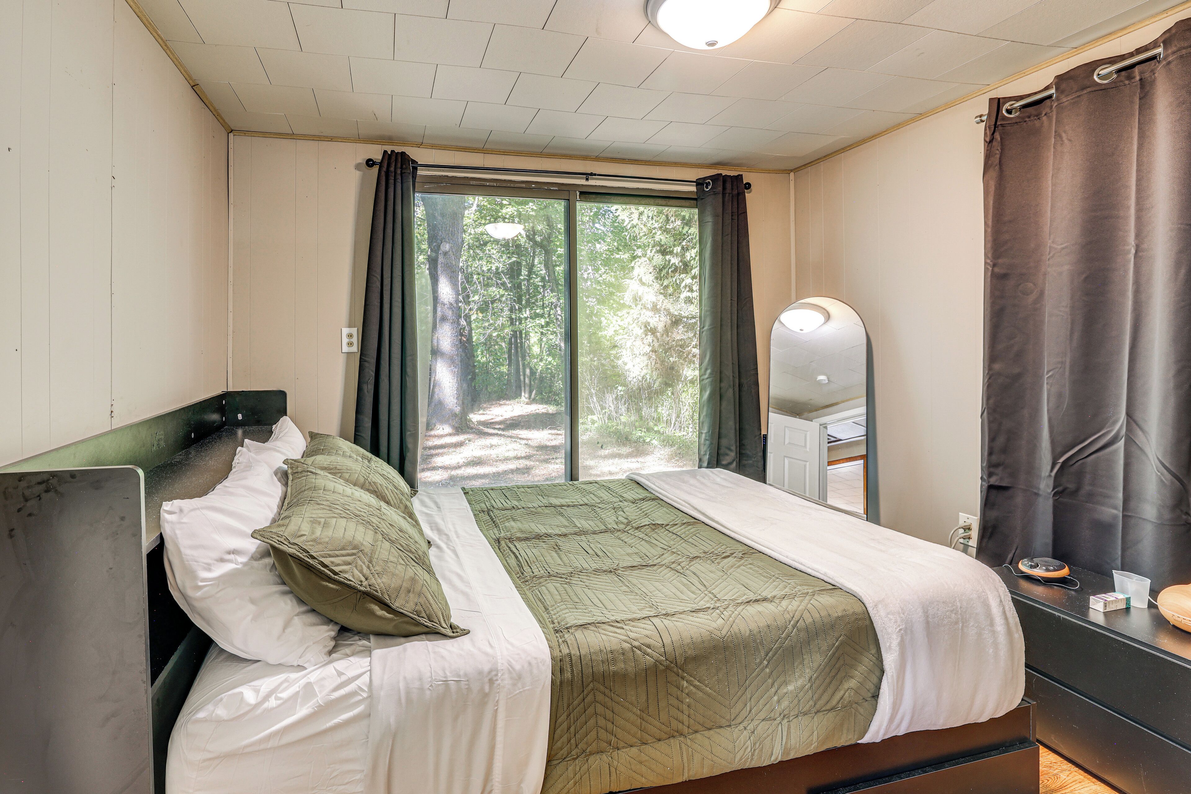A bedroom with a bed, a mirror, and a window with curtains.