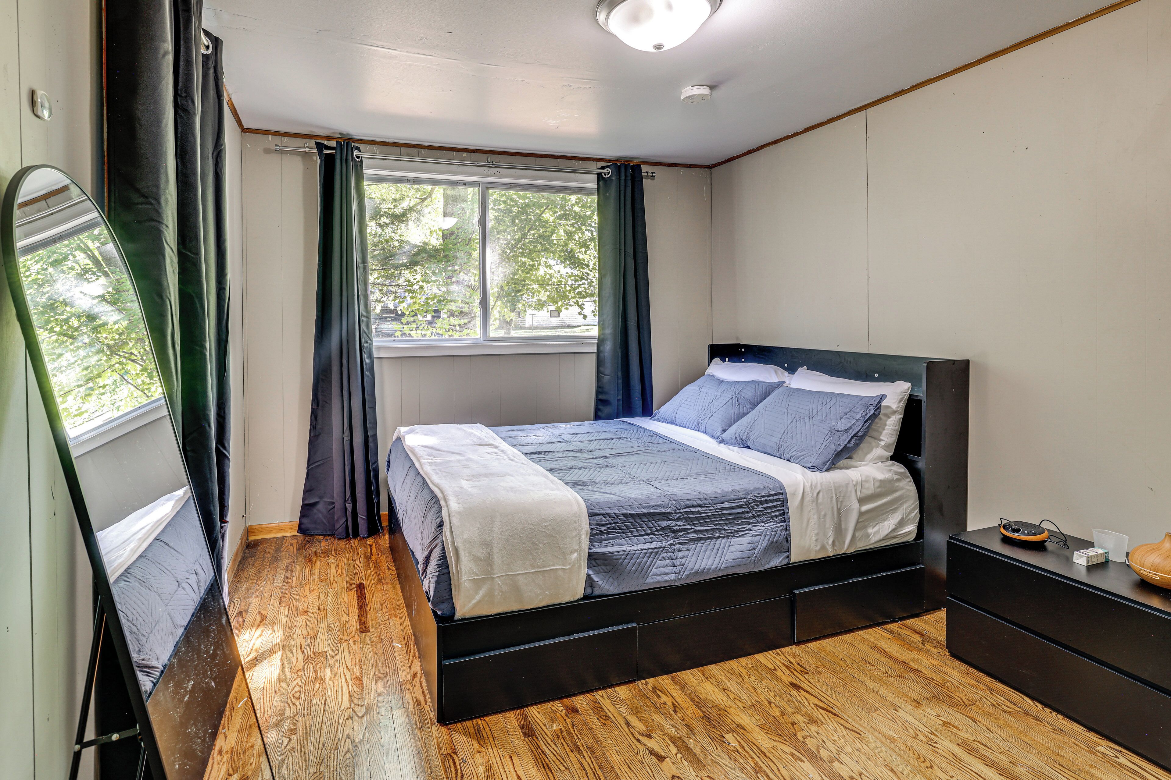 A bedroom with a bed, a nightstand, a mirror, and a window with curtains.