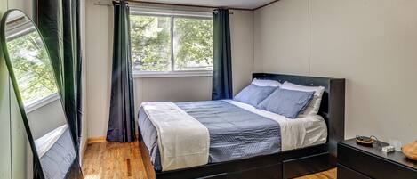 A bedroom with a bed, a nightstand, a mirror, and a window with curtains.