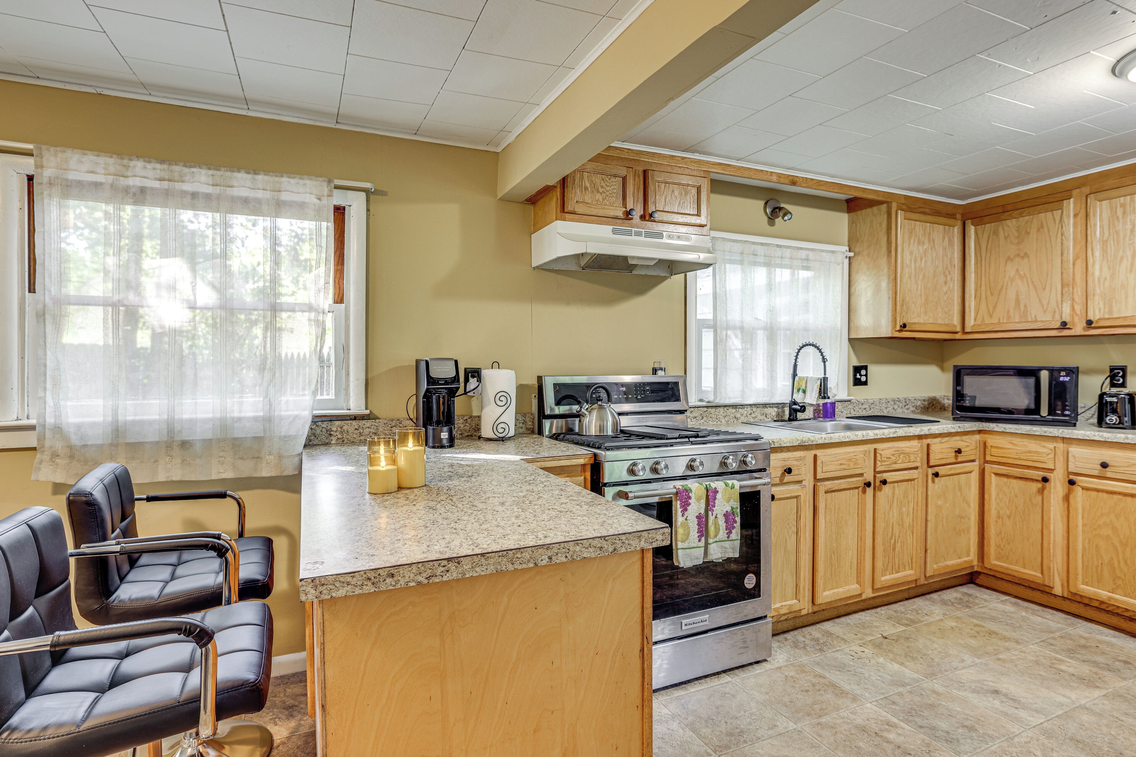 A kitchen with wooden cabinets, a stove, a microwave, and a sink. There are chairs and a coffee maker.