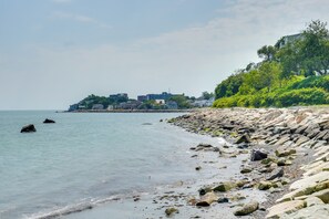 Eine Küstenlandschaft mit felsiger Küste, ruhiger See und einer Ansammlung von Gebäuden auf einem Hügel.