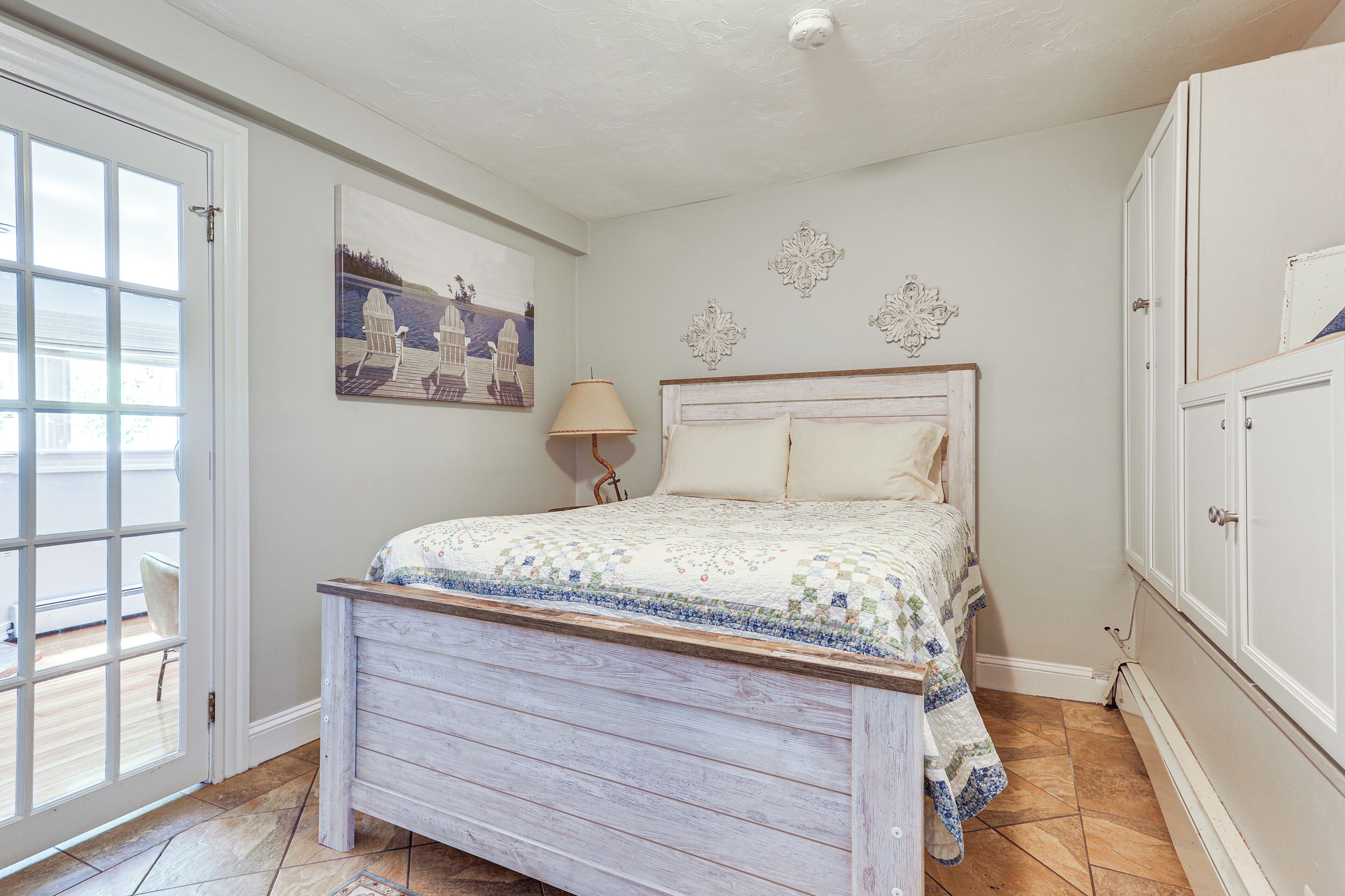 A bedroom with a bed, a door, a lamp, and a painting on the wall.
