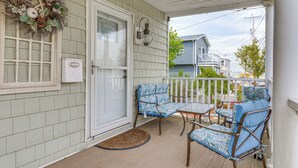 Une véranda avec deux chaises bleues à motifs et une petite table, une guirlande décorative accrochée au mur, et une porte avec un panneau de verre.