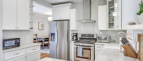 A modern kitchen with white cabinetry, a stainless steel refrigerator, a built-in oven, and a microwave.