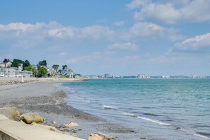 A beach with a concrete walkway, calm water, and buildings in the background.