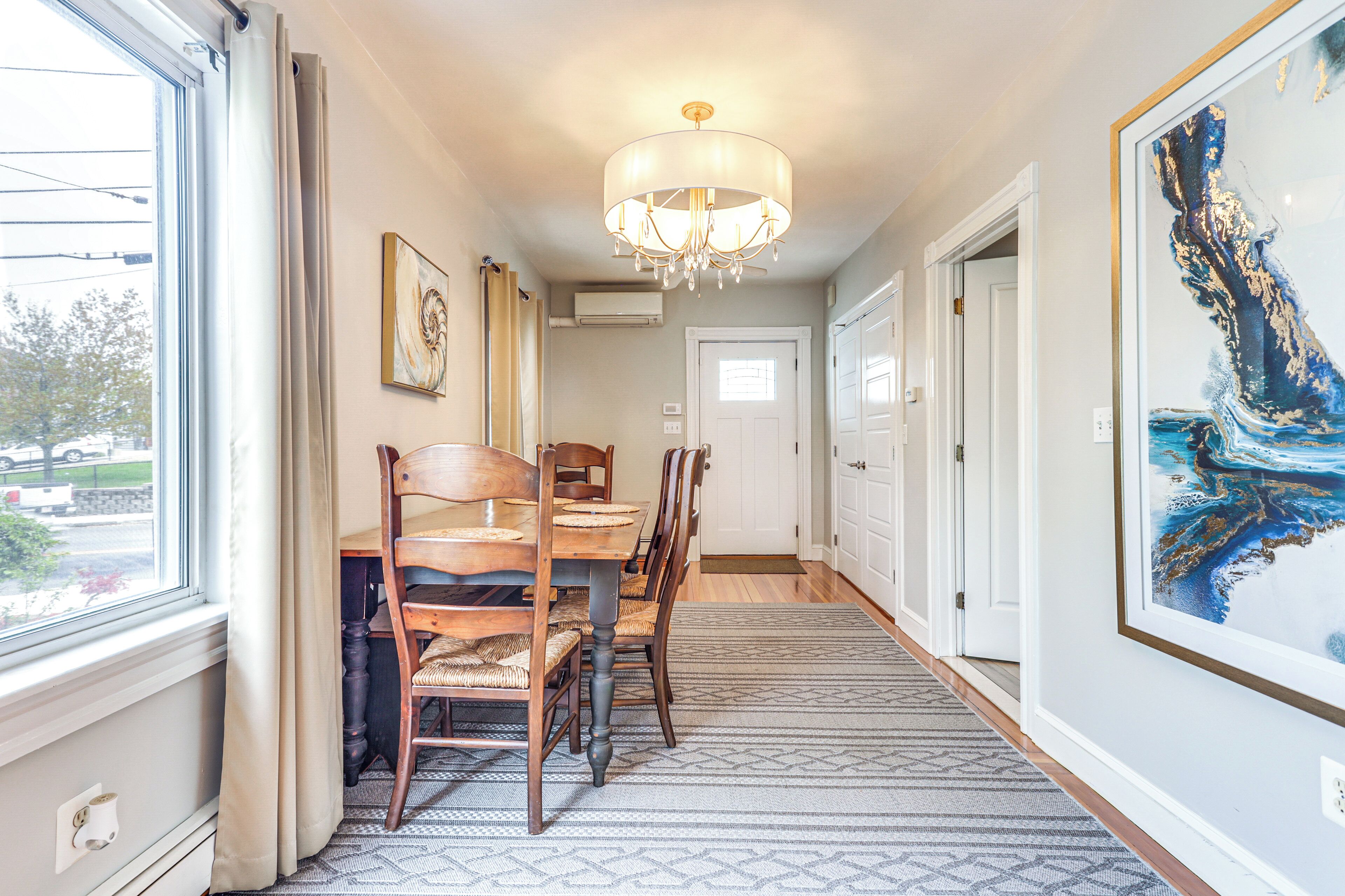 A hallway with a dining table and chairs, a chandelier, and a large painting on the wall.