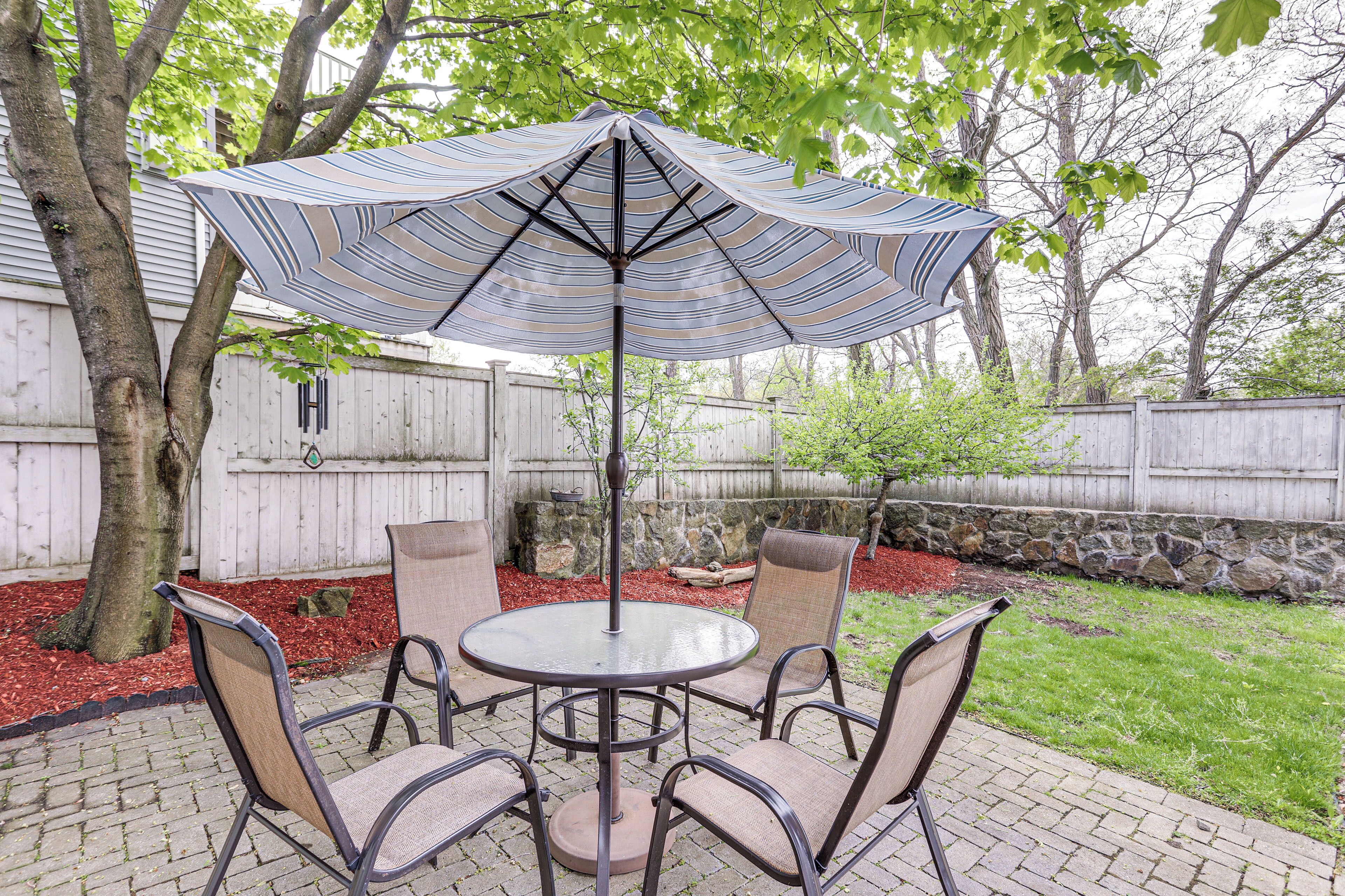 Une terrasse avec une table ronde et quatre chaises, un parasol et une clôture en bois en arrière-plan.