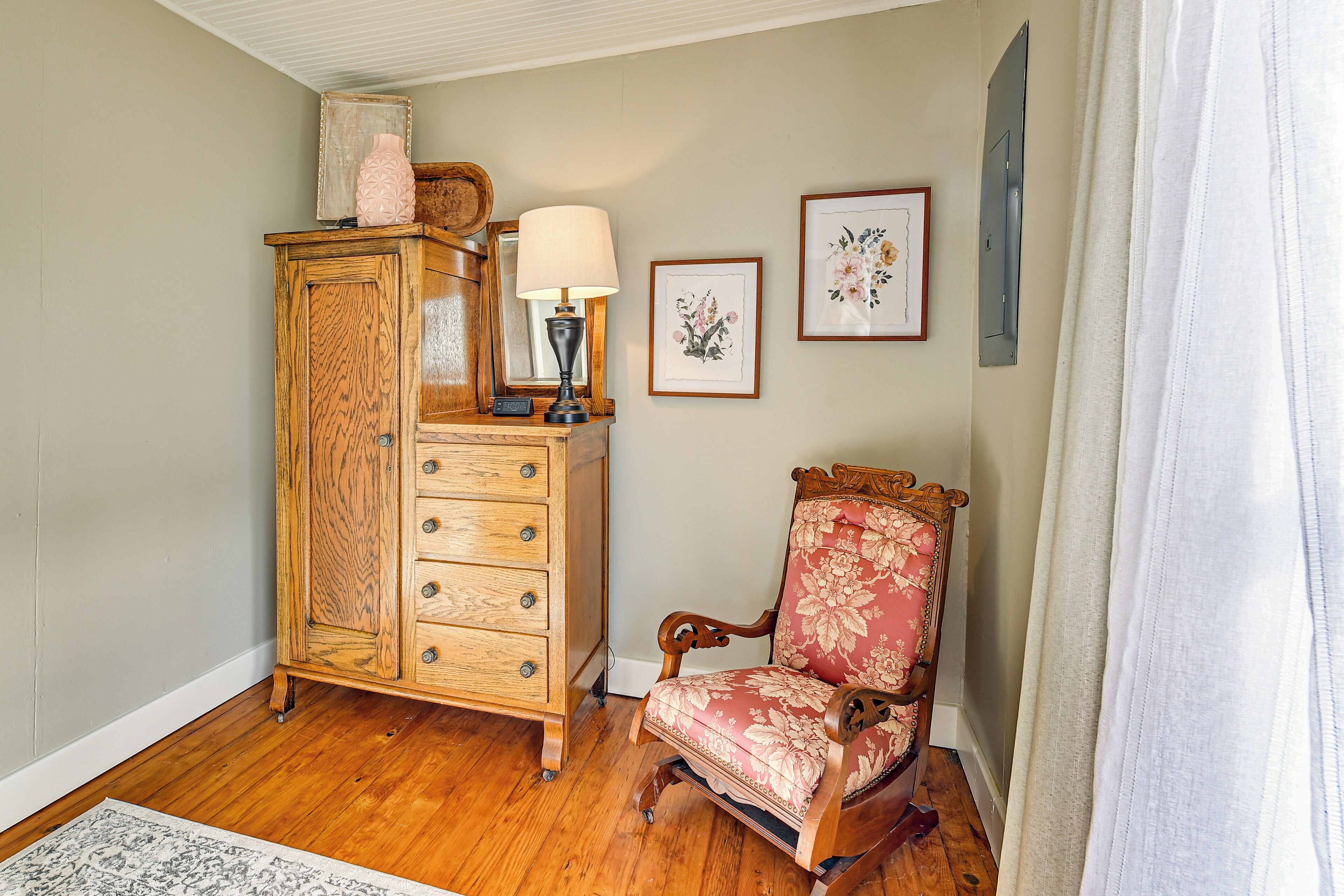 Un mueble de madera con cajones, una silla con tapicería floral y una obra de arte floral enmarcada en la pared.