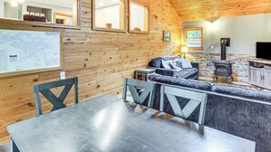 A cozy cabin interior with wooden walls, a stone fireplace, a sofa, and a dining area. - Sauna + Deck: Wooded Cabin on Lake Vermilion! (Tower)