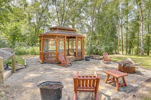 A gazebo with wooden chairs and a table, surrounded by a stone patio and a forested area. - Charming Couples Cabin on 40 Acres in Zanesville (Zanesville)