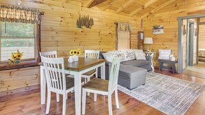 A wooden cabin interior with a dining table, chairs, a sofa, and a rug.