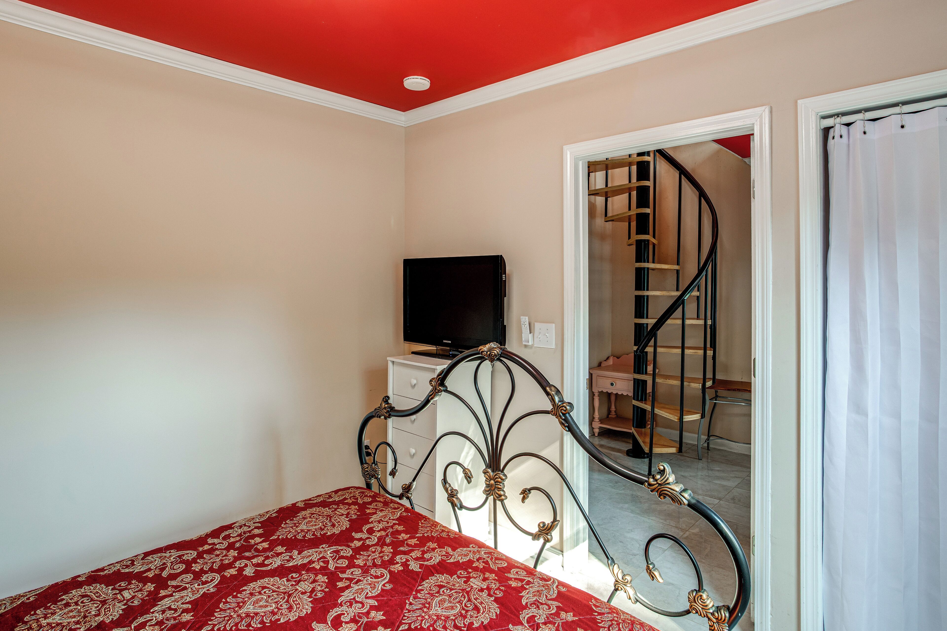 Ein Schlafzimmer mit einem Bett, einem Fernseher auf einer Kommode und einer Treppe, die zu einer oberen Etage führt.
