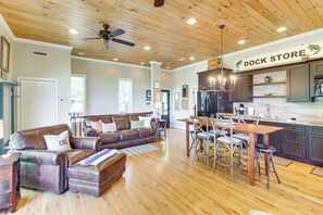 A spacious living room with a leather sofa, wooden dining table, and a kitchen area with a sign reading "DOCK STORE". - Lake View Home in Silver Point: Walk to Marina (Silver Point)