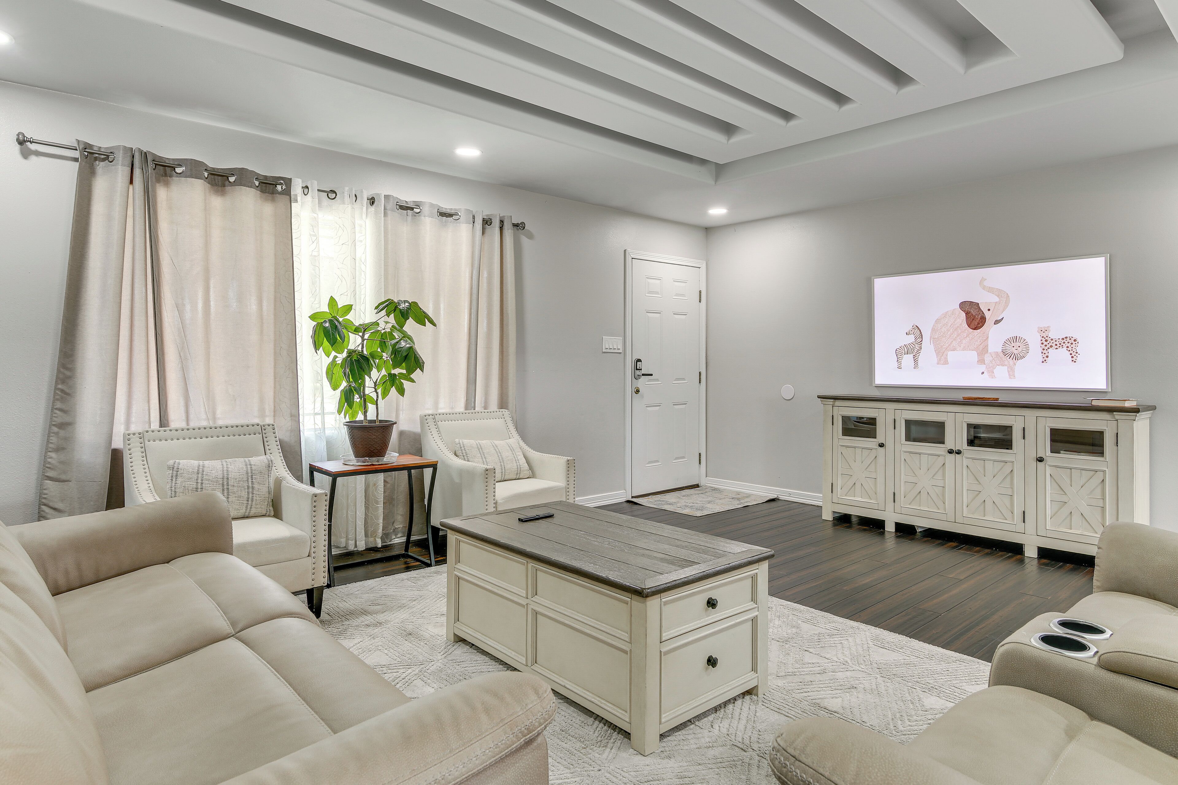 A modern living room with a beige sofa, a coffee table, a potted plant, and a white cabinet with glass doors.