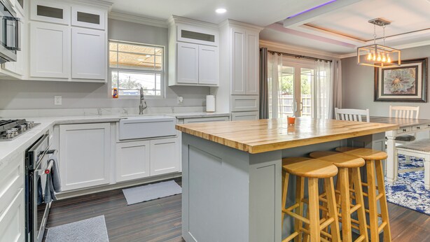 A modern kitchen with white cabinetry, a wooden island with bar stools, and a pendant light. - Fenced Yard: Home < 1 Mi to Mayor Pablo Peña Park (Weslaco)