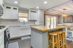 A modern kitchen with white cabinetry, a wooden island with bar stools, and a pendant light. - Fenced Yard: Home < 1 Mi to Mayor Pablo Peña Park (Weslaco)