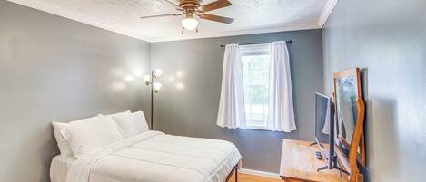 A bedroom with a bed, ceiling fan, bedside table, and a TV mounted on the wall.